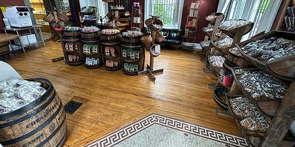 Inside the candy shop with shelves filled with candy, wood floor and a stair case in the background.